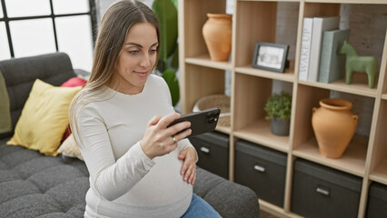 Pregnant hispanic woman using smartphone in a cozy living room.