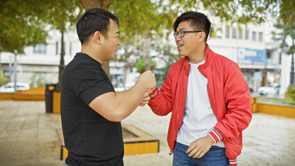 Two asian men casually greeting each other with a handshake in a city park setting.