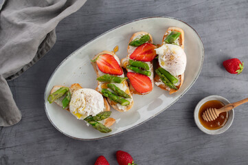 Toast bruschetta with grilled asparagus, poached egg, strawberry and fresh cream cheese. Sourdough bread with vegetables and egg. Food photography. Healthy breakfast, brunch. Summer food