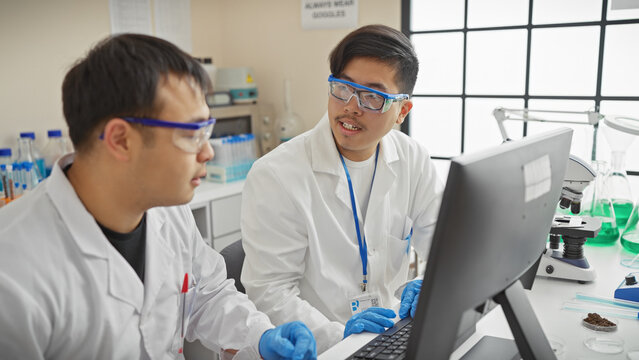 Two men in lab coats discussing data on a computer in a modern laboratory setting