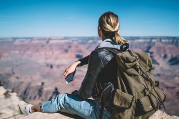Young female tourist looking at beautiful scenery landscape of Grand Canyon sitting on peak...
