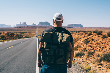 Young hipster guy with rucksack walking near asphalt road lead to National park on southwest, back...