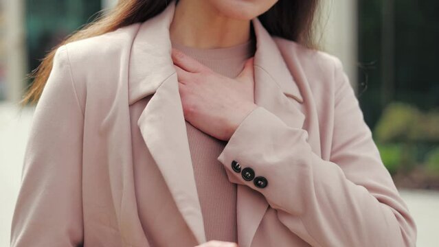 Lamentable brunette female holding personal smartphone while touching chest because having respiratory problems. Upset caucasian woman preparing to call doctor and making appointment outdoors.