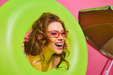 Portrait of young woman holds neon-green inflatable ring and smiles brightly peeking out of it on...