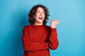 Photo of attractive excited guy wear red sweater showing thumb emtpy space isolated blue color...