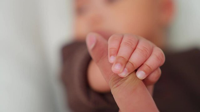 Newborn baby playing with mother's hand and finger lying on bed. baby little cute reaching touching mom finger. Baby holding parents finger. Parent holding newborns hand. mama takes care child.