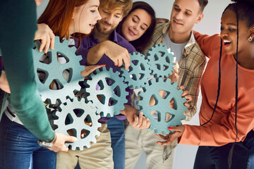 Team of diverse people connecting mechanical cogs. Group of smiling male and female teammates...
