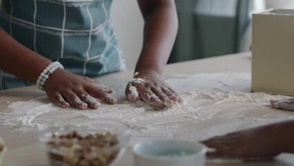 Close-up of hands of unrecognizable black woman and children dusting flour over kitchen table surface going to prepare dough-based dish or knead pastry for bread