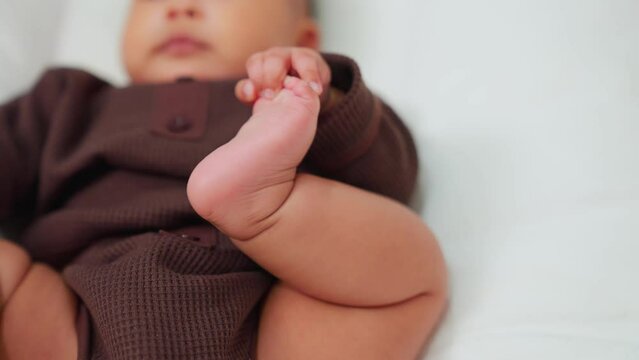 Chubby baby of asian Close up of sweet beautiful newborn baby lying on bed sheets, plays touches toes laughs smile. Carefree healthy babyhood, healthcare and paediatrics care concept