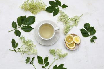 Cup of herbal elderflower tea. Elderflowers, green leaves and fresh lemon fruit slices on old white...