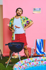 Man posing in studio with inflatable pool and cooking barbeque sausages for picnic. Summer activities. Concept of pop art, remote work, travelling, party, recreation, lifestyle, fashion and style.