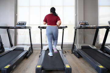 Back view of Asian overweight women in sportswear running on treadmill in fitness club. Weight loss...