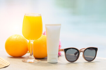 Free space bottle mock up products. Vitamin C skincare with fresh orange juice, hat, pineapples, and sunglasses near the swimming pool. travel vacation accessory.