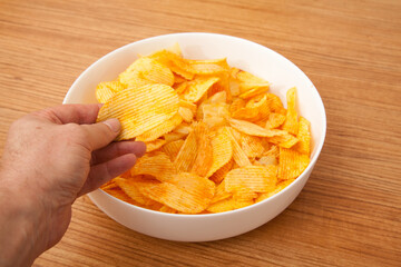 There are potato chips in a white plate, a caucasian person is holding potato chips in his hand