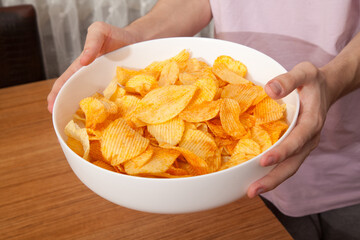 Caucasian person in pink t-shirt holding plate full of potato chips and preparing to eat