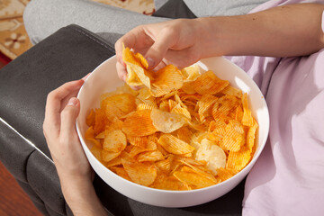 Caucasian person in pink t-shirt holding plate full of potato chips and preparing to eat
