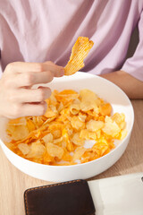 Caucasian person in pink t-shirt holding plate full of potato chips and preparing to eat