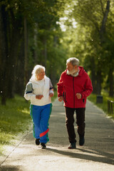 Fototapeta premium Elderly and active man and woman, positive couple in sportswear energetically jogging in early morning park, training. Concept of sport, aging, active and healthy lifestyle, health care