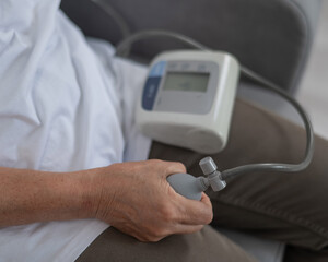 Mature Caucasian woman measuring blood pressure while sitting on sofa at home. 