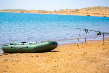 An inflatable boat moored on the shore of a lake. A green boat on the sandy shore of a pond....