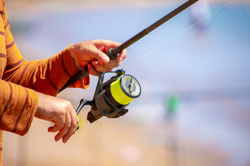 Fisherman's hands turning a reel on a fishing rod. Close-up of fishing reels. Fishing on the shore...