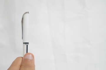 A pen is being held up in front of a white background