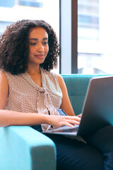 Businesswoman Sitting In Lobby Of Modern Office Building Working On Laptop