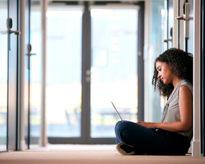 Businesswoman Sitting On Floor In Corridor Of Modern Office Building Working On Laptop