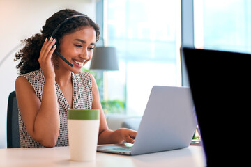 Woman Wearing Headset Sitting At Desk With Laptop Working In Office Call Centre Team Taking Call