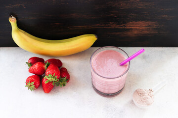Strawberry and banana smoothie, protein drink in a glass, measuring scoop with whey protein powder,...