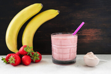 Strawberry and banana smoothie, protein drink in a glass, measuring scoop with whey protein powder,...