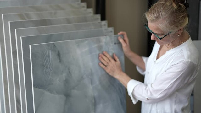 Mature woman with her hand touching a sample of marble stone for flooring and countertops in a design center store for a home renovation redecorating project.