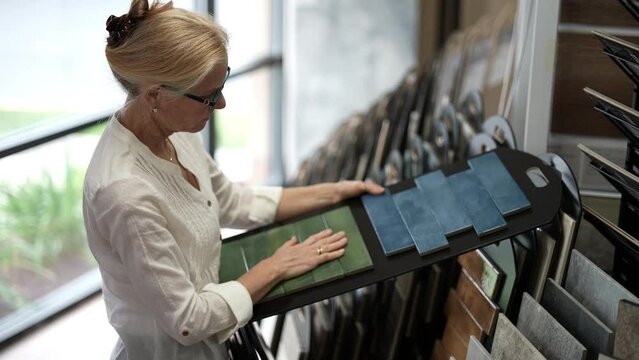 Happy mature woman touching samples of floor and wall tiles in a design center store for a home renovation redecorating project.