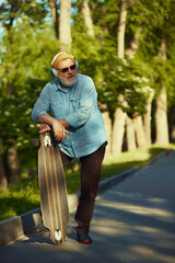 Senior Style. Elderly man in stylish clothes, beanie hat, headphones and sunglasses standing in...