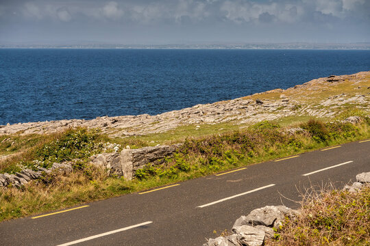 A road with a view of the ocean. The sky is cloudy and the water is blue. Burren, Ireland. Stunning nature scenery with rough stone terrain. Irish nature landscape.