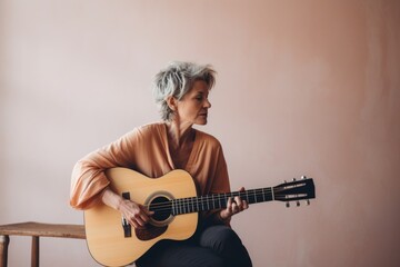 Portrait of a satisfied woman in her 50s playing the guitar over minimalist or empty room background