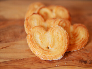 Delicate cookies made in heart shape are arranged in a stack with wooden board underneath. French style pastry sweet desert. Bakery product. Selective focus. Warm color.