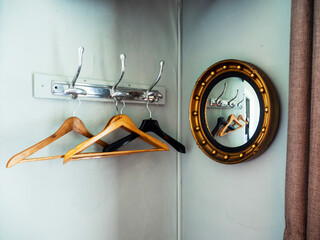 A mirror is hanging on a wall next to a rack of empty wood clothes hanger. Staying in a hotel...