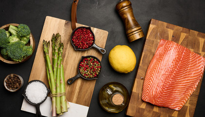 A piece of raw trout fillet on a wooden board, next to asparagus and broccoli.