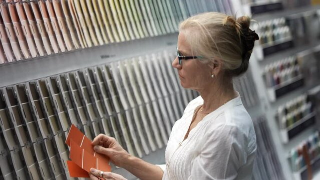 Happy mature woman trying to match paint color swatches while shopping for home redecorating renovation project, in a hardware store.