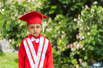 portrait of bored little latin boy, dressed in red graduation gown