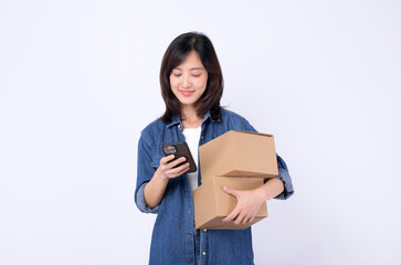 Naklejka premium asian woman wearing denim jean holding parcel box while using mobile phone isolated on white studio background, Delivery courier and shipping service concept.