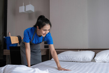 The hotel housekeeper in the room was cleaning the bed and preparing the bedding.