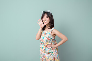 Happy Asian woman with sun glasses shouting above casual dress poses against pastel green...
