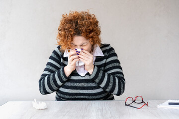A woman with a red head and black and gray striped sweater is blowing her nose.