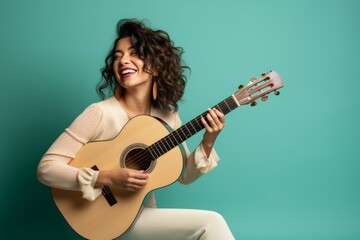 Portrait of a cheerful woman in her 30s playing the guitar isolated in solid color backdrop
