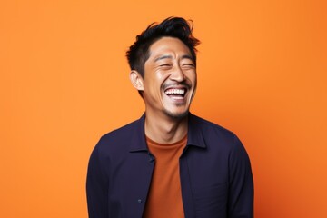 Obraz premium Portrait of a happy asian man in his 30s laughing on solid color backdrop