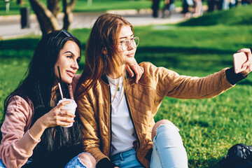 Cheerful best friends posing for making selfie on smartphone camera spending time together in park.Happy hipster girls in trendy outfit taking photos for uploading in social networks via mobile device
