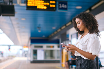 Businesswoman Commuting On Train Platform Using Mobile Phone For Travel Information Or Social Media