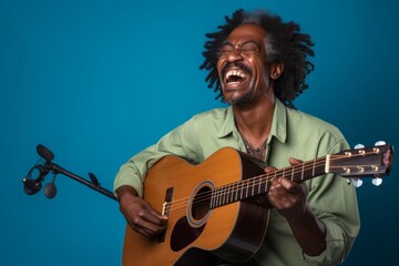 Obraz premium Portrait of a happy afro-american man in his 40s playing the guitar while standing against solid color backdrop